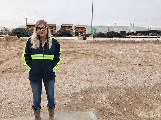 Female mine operator in front of haul trucks