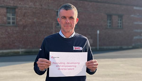 Anthony at Coudekerque operations celebrating International Women's Day. He's holding a sign that says: Recruiting, developing, and empowering diverse talent.