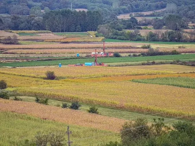 Fields with plants from heightened view showing drill rigs in the distance.