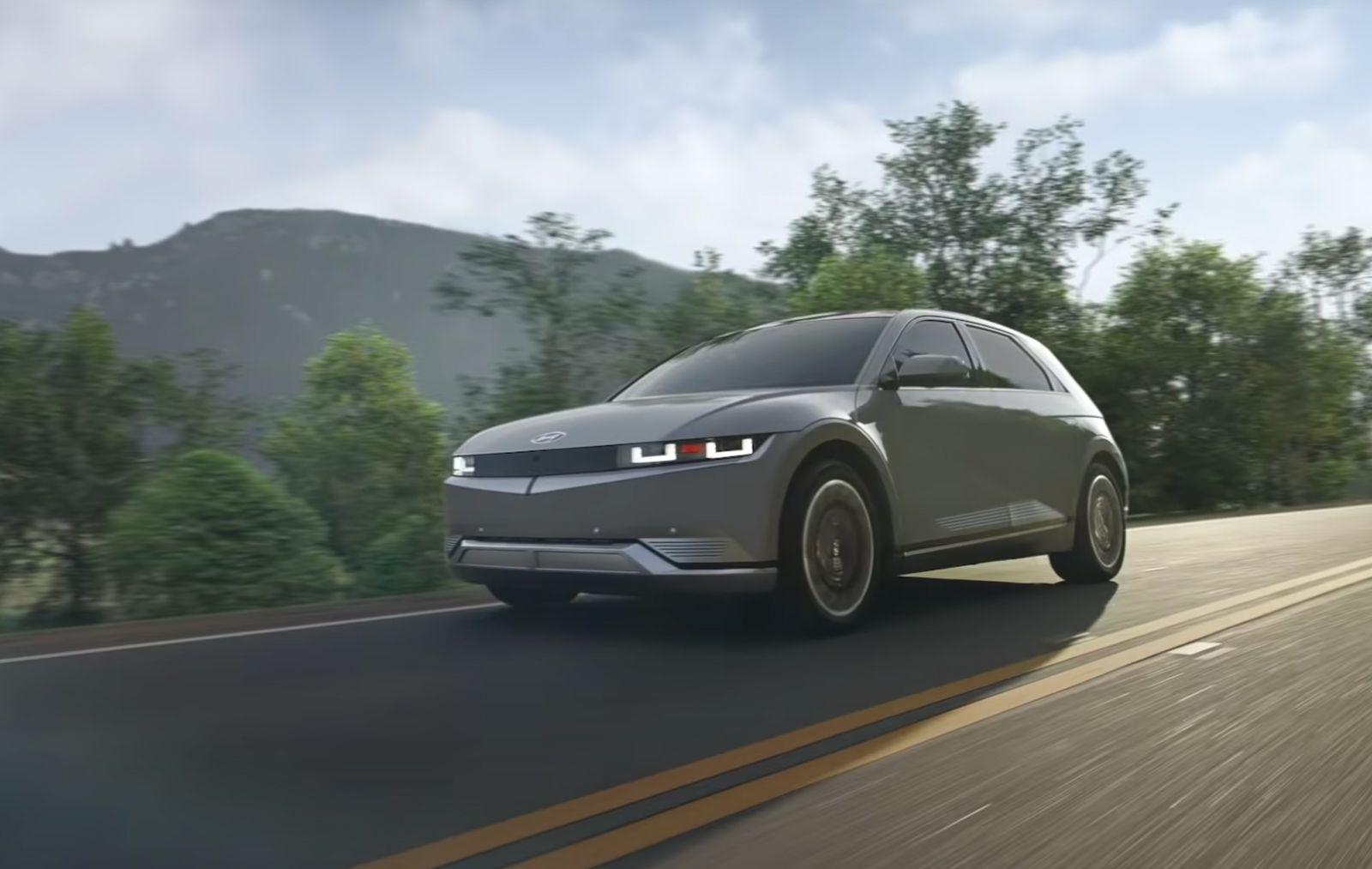 a grey hyundai ioniq 5 driving on a road surrounded by trees