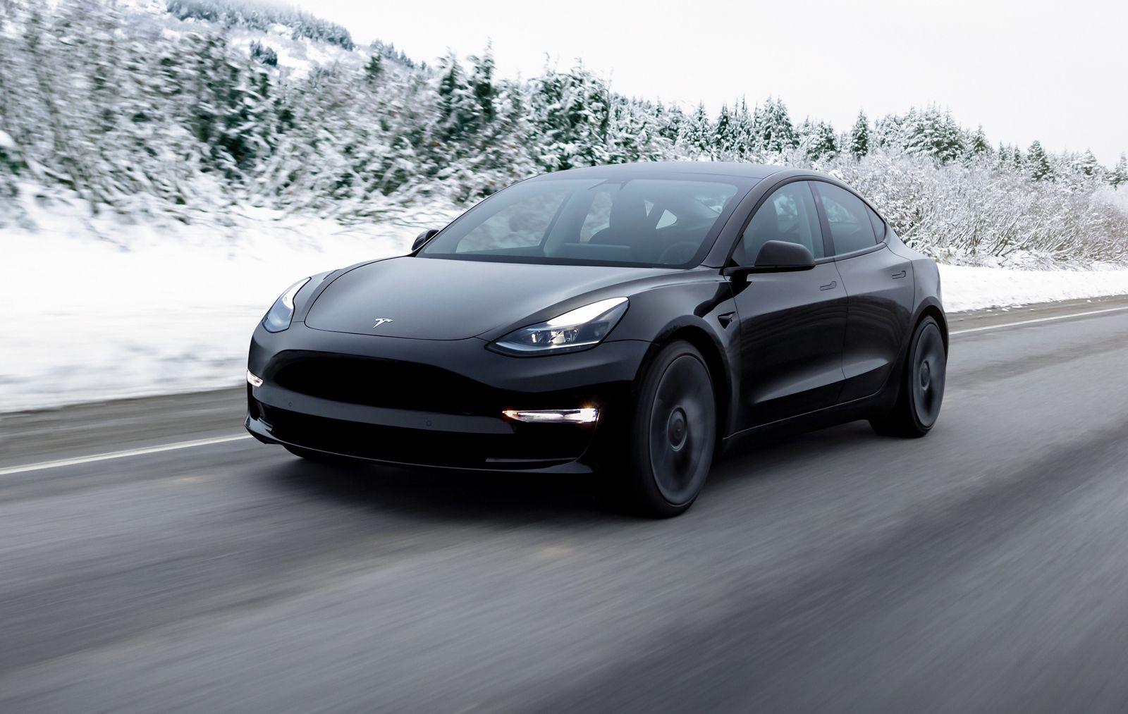 a black Tesla Model 3 driving on a clear road in the snow