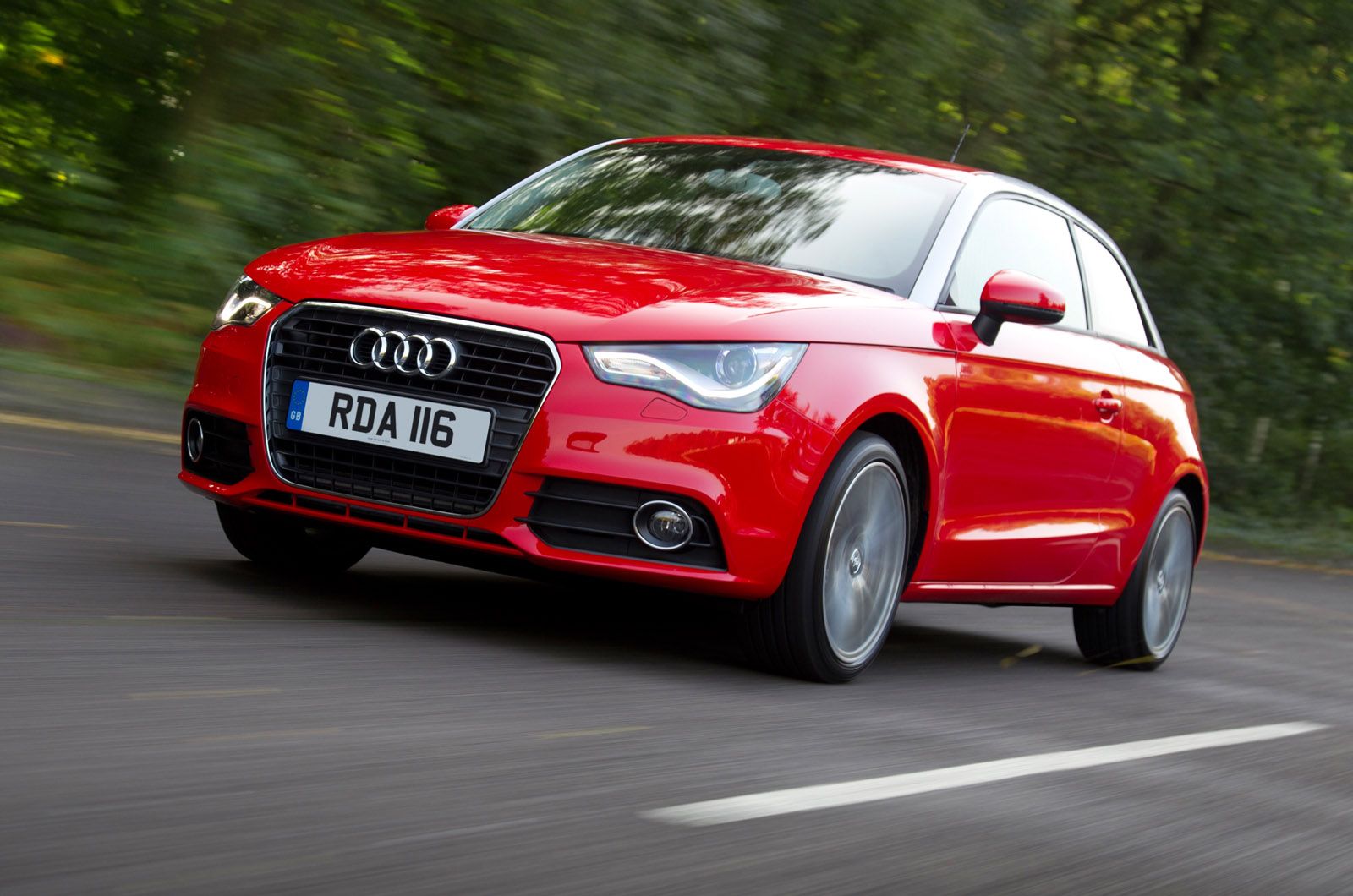 Red Audi A1 in motion on a road with blurred trees in the background, highlighting its sleek design and dynamic presence.
