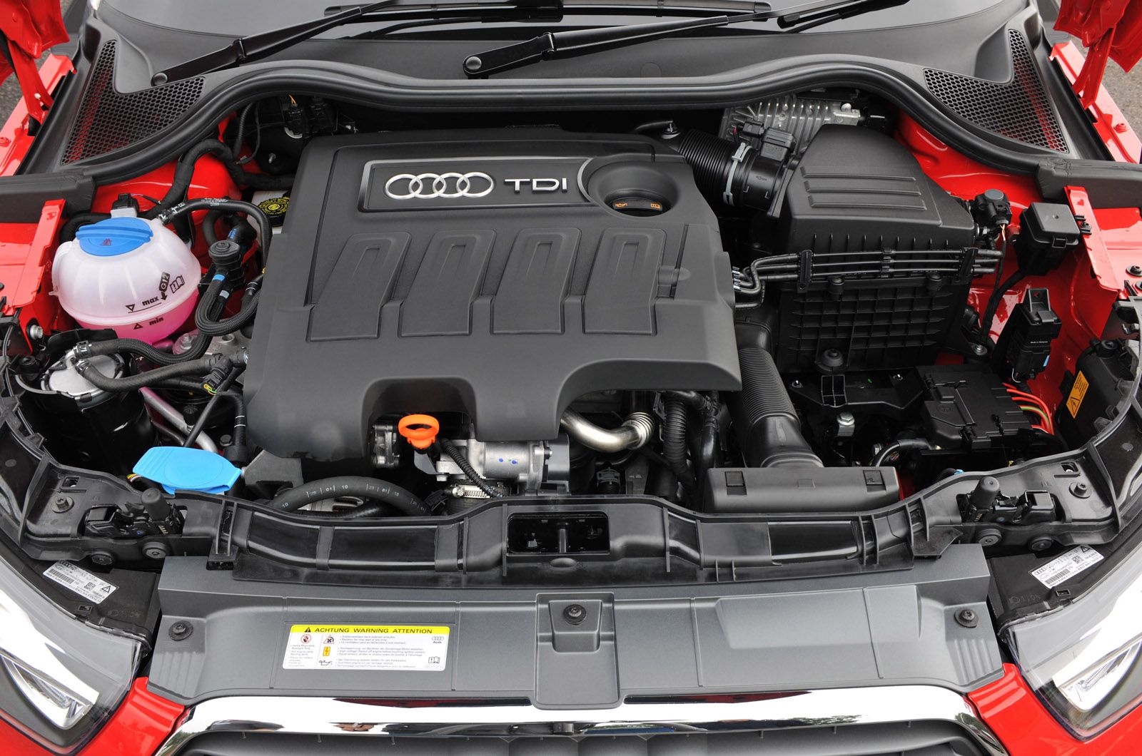 Close-up of an Audi TDI engine bay, showing engine cover, various hoses, and components inside a red car.