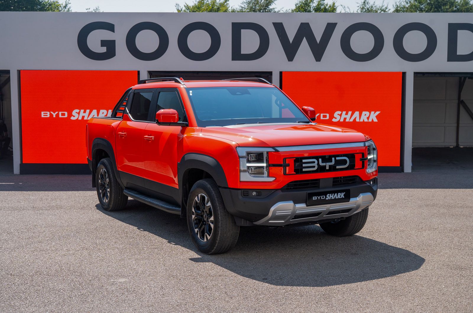 Red BYD Shark pickup truck parked in front of a “Goodwood” sign, with bright orange promotional banners in the background.