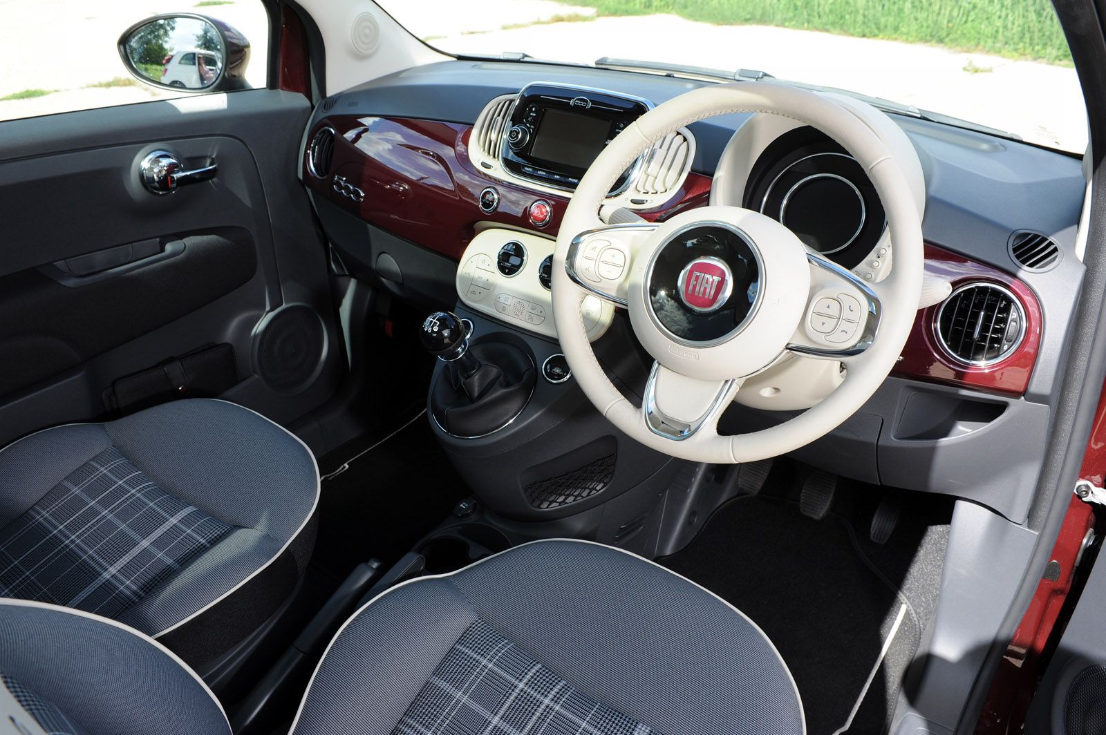 Interior of a Fiat car with a two-tone steering wheel, a manual gear shift, and dual-tone seats with plaid pattern.