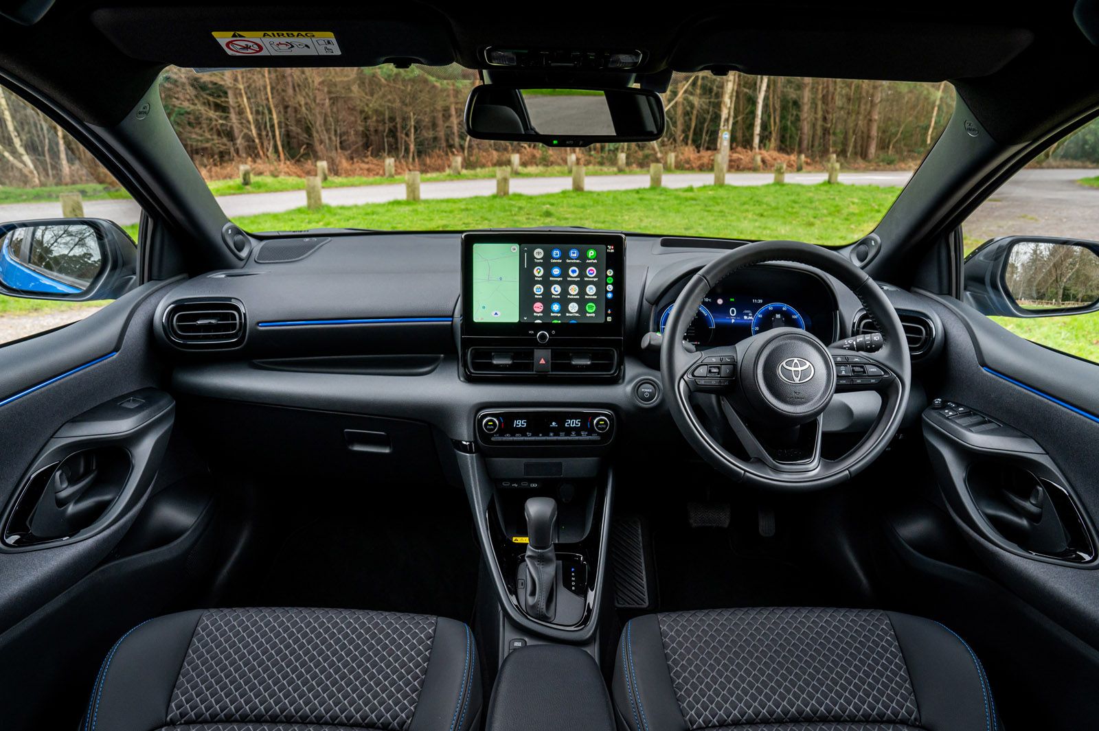 Car interior with a sleek dashboard featuring a touchscreen, steering wheel, and digital display, set against a scenic outdoor background.