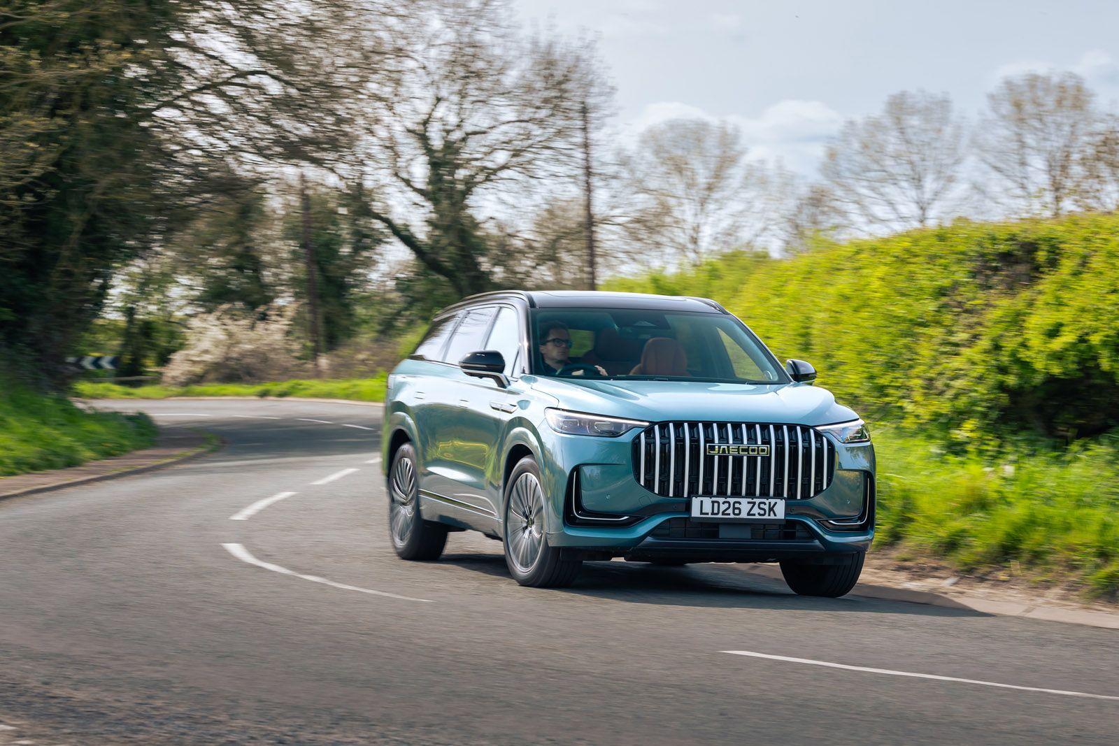 Blue SUV driving on a winding country road with greenery and trees in the background under a clear sky.