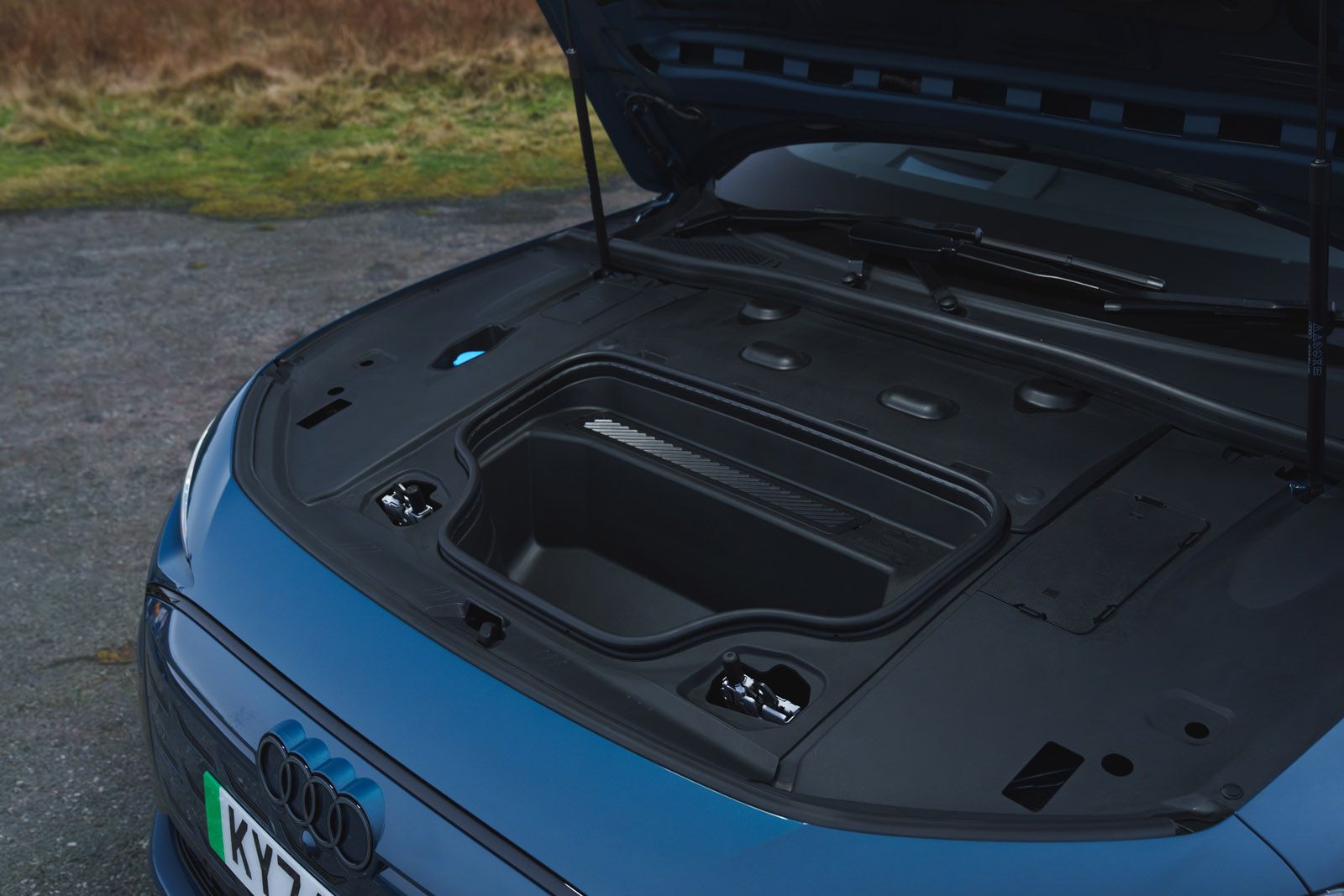 Open front trunk of a blue electric car, showing a spacious compartment. The hood is lifted, revealing a clean and sleek design.