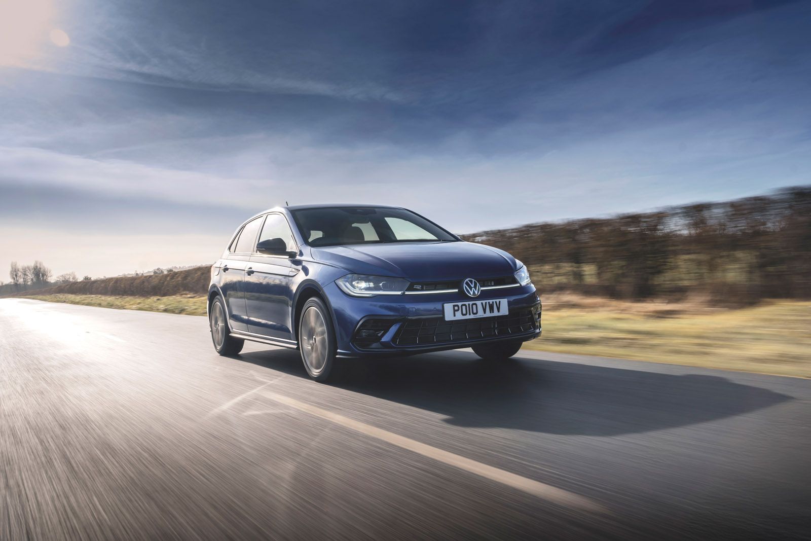 Blue Volkswagen car driving on a country road under a clear sky, with motion blur from speed.