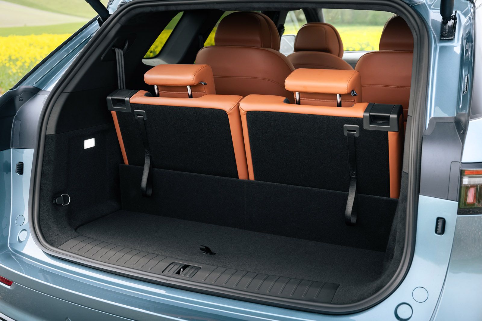 Open trunk of a blue SUV with two brown rear seats folded up, showcasing ample cargo space.