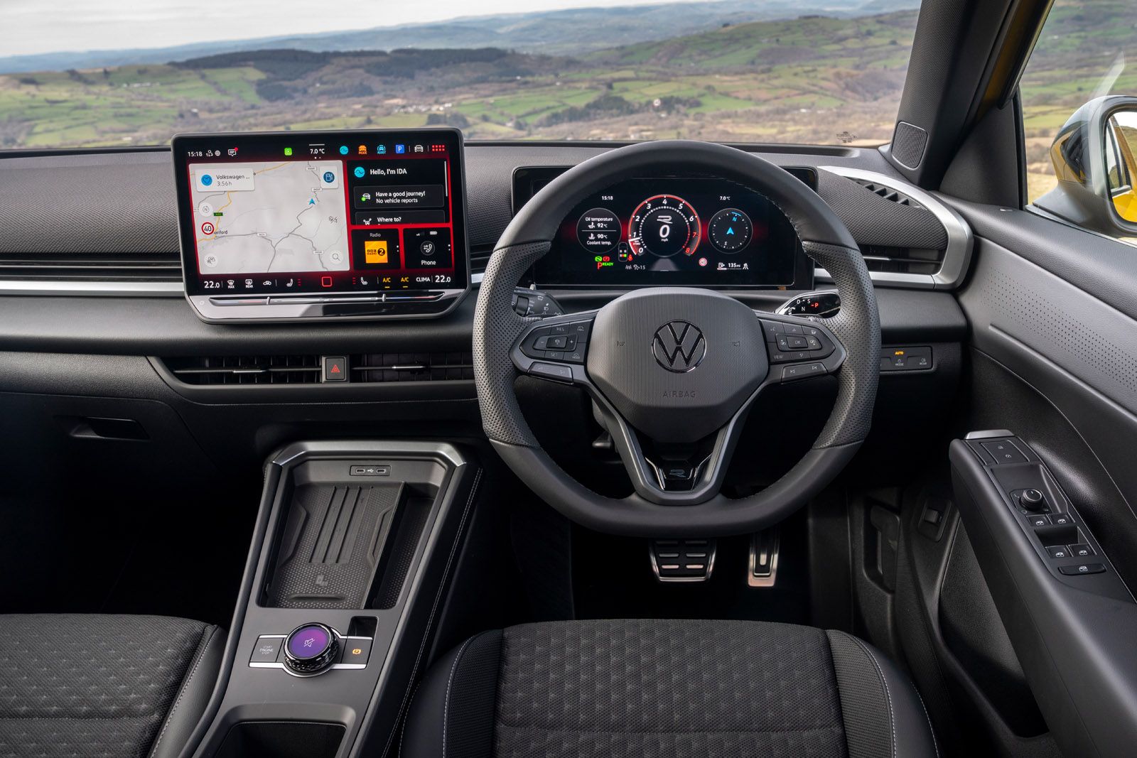 Car interior with a modern dashboard, digital displays, and steering wheel, set against a scenic landscape background.