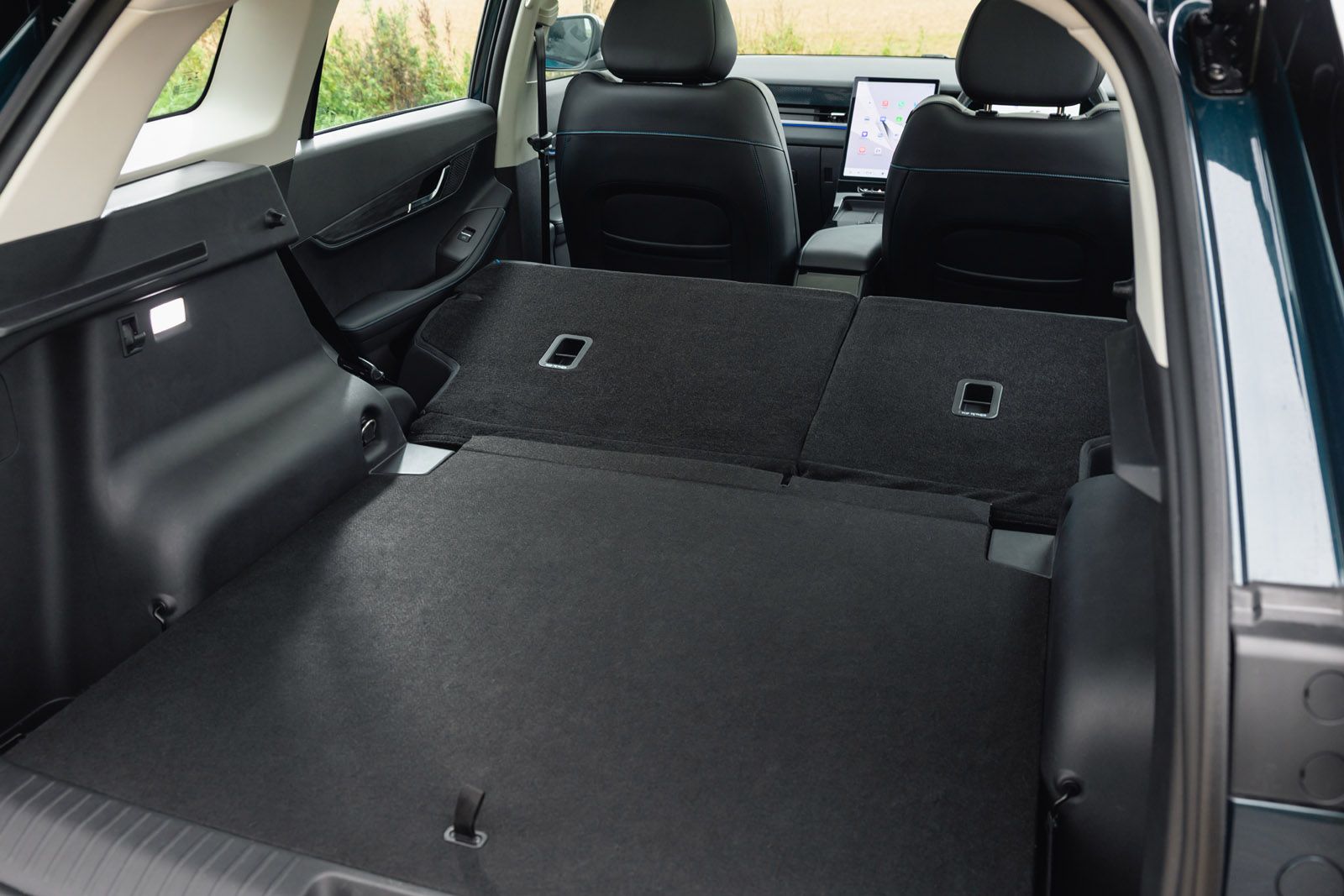 JAECOO E5 interior showing the back seats folded flat, with a spacious, empty cargo area and a visible touch-screen dashboard in the front.