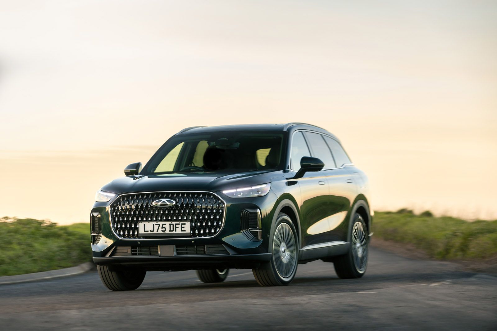 A sleek black SUV driving on a scenic road with a blurred background of greenery and a soft sky.