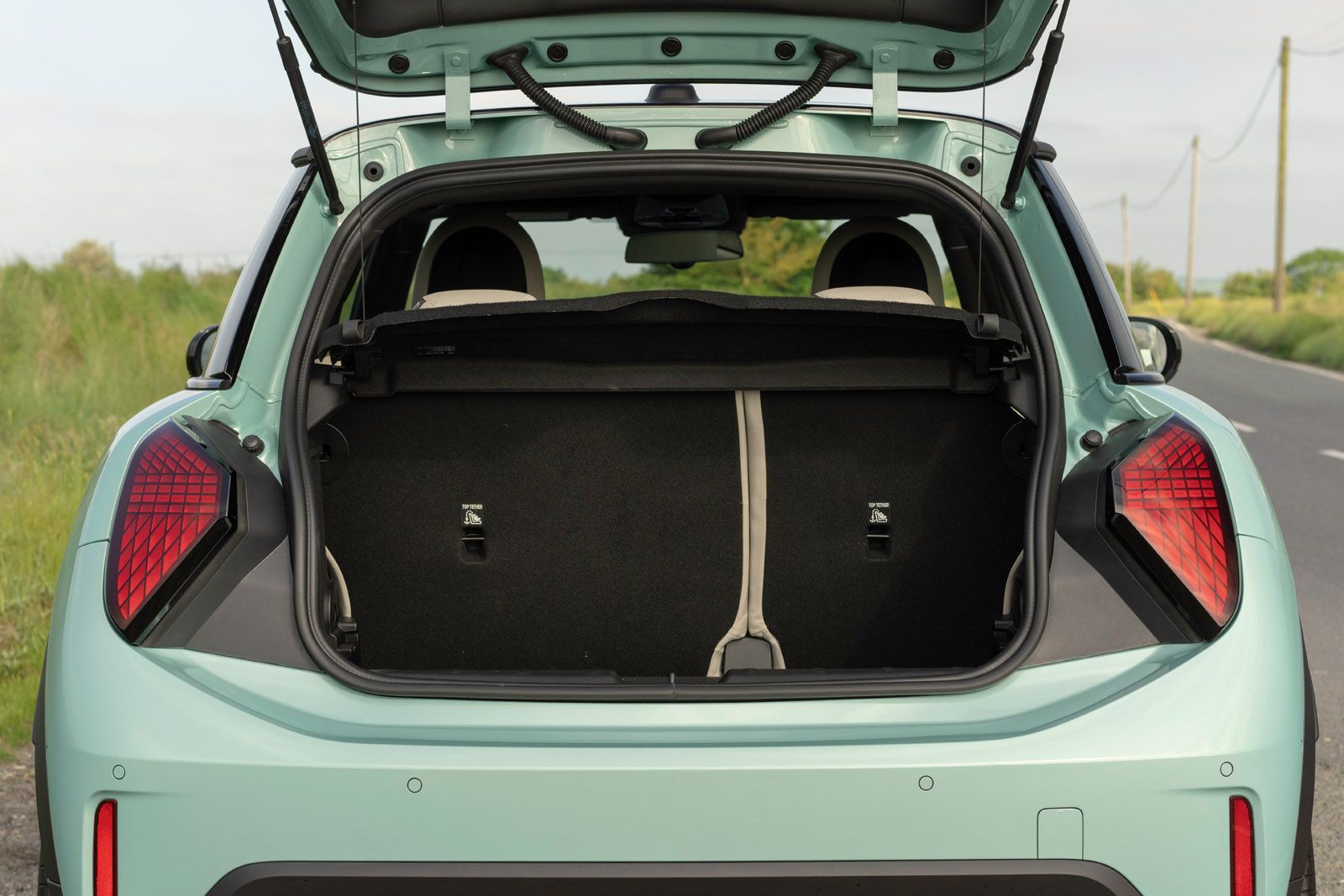 Open trunk of a light blue SUV parked on a roadside, showing a spacious cargo area with the rear seats visible against a grassy landscape.