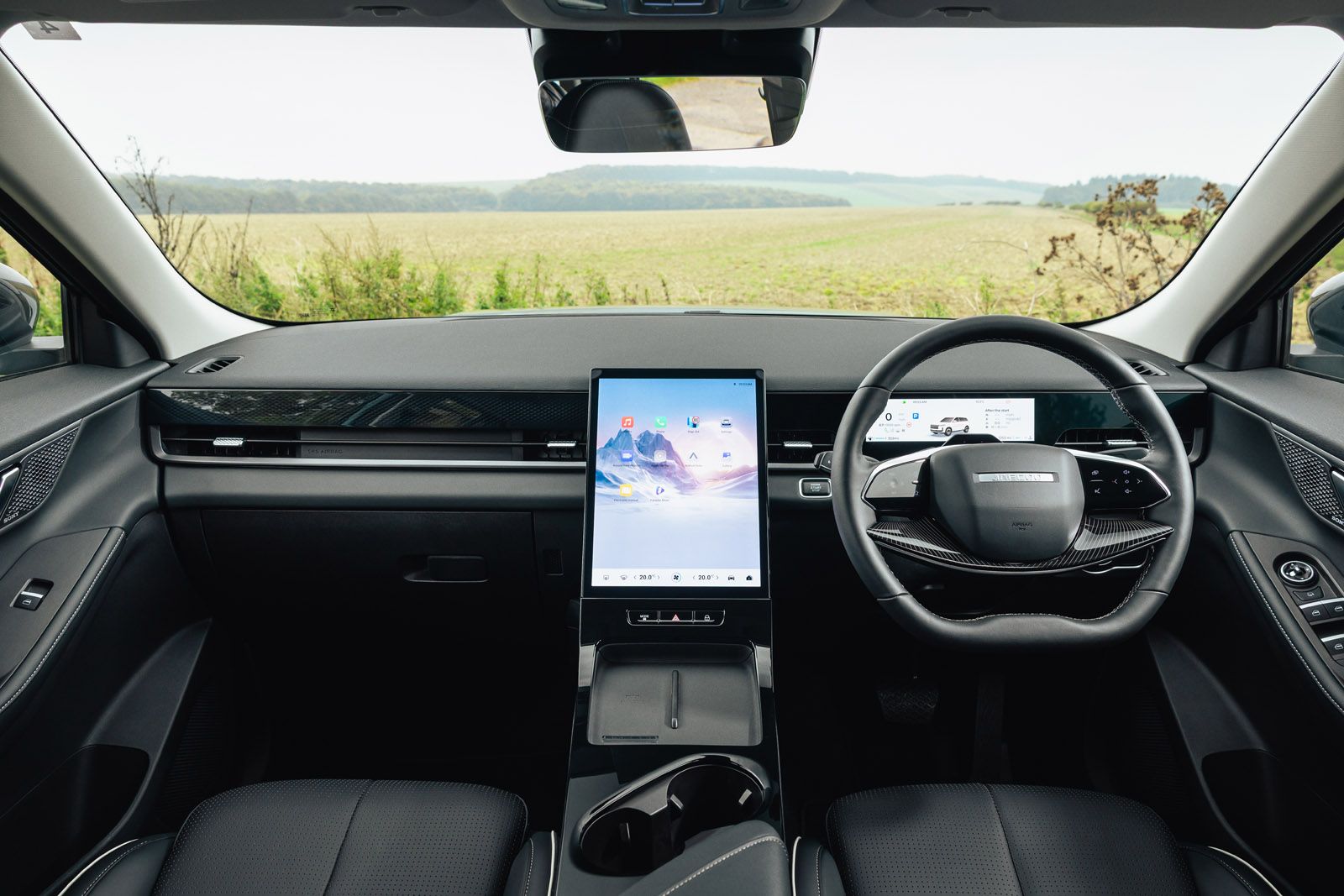 JAECOO 5 interior with a sleek dashboard, large central touchscreen, digital display behind the steering wheel, set against a countryside view.