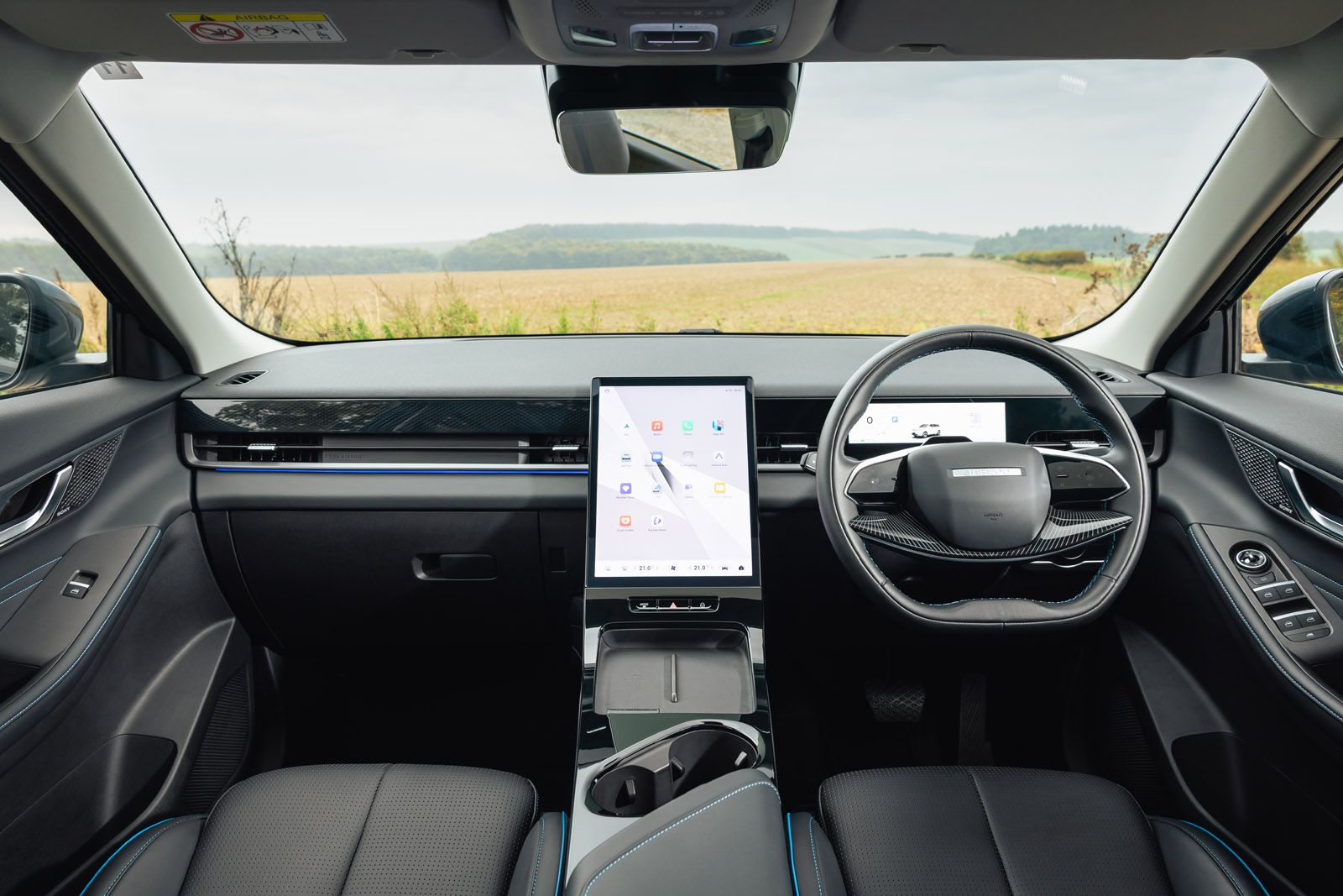 JAECOO E5 interior with a large central touchscreen, sleek steering wheel, and expansive countryside view through the windshield.