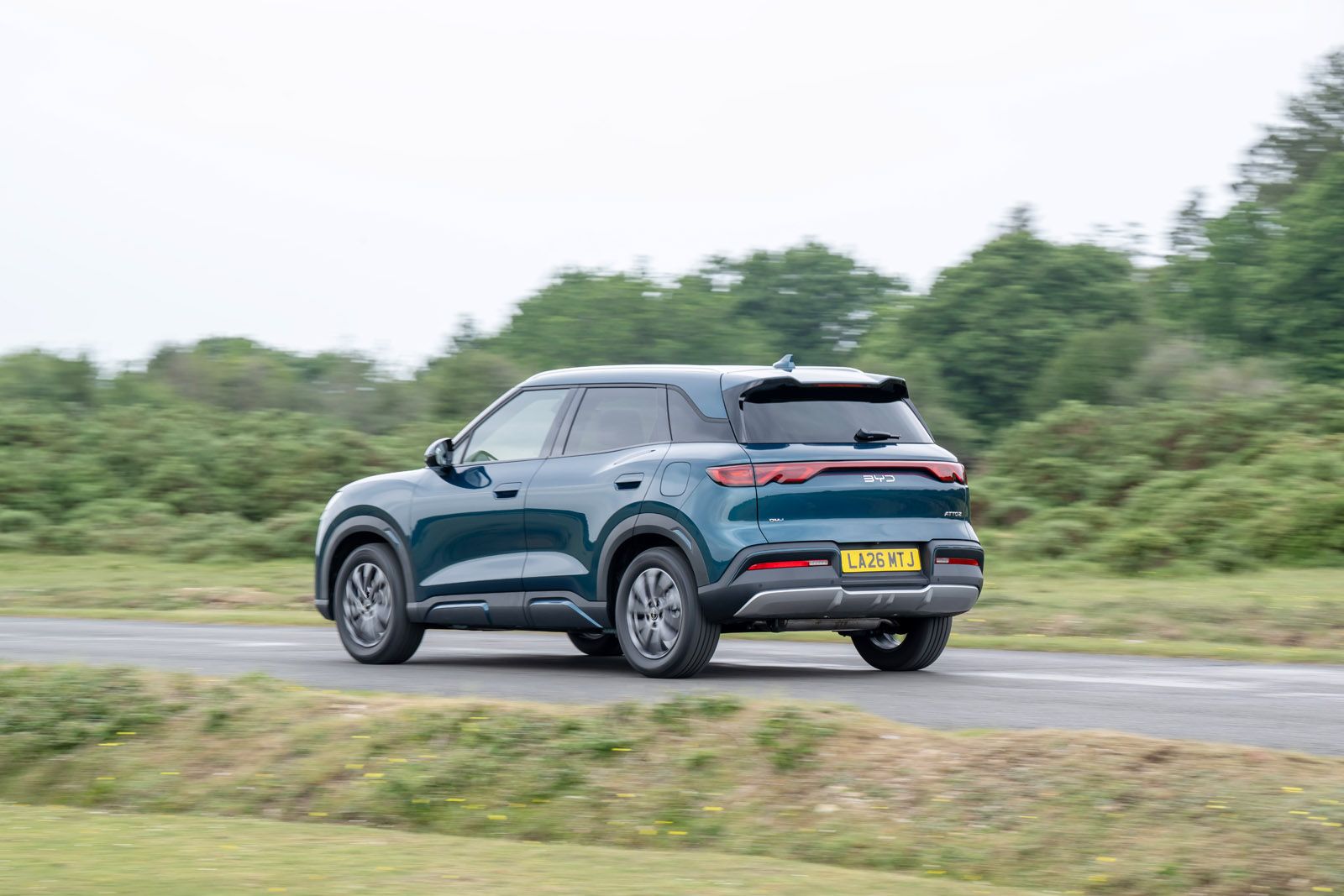 A blue SUV driving on a road with greenery in the background, captured from the rear left side.