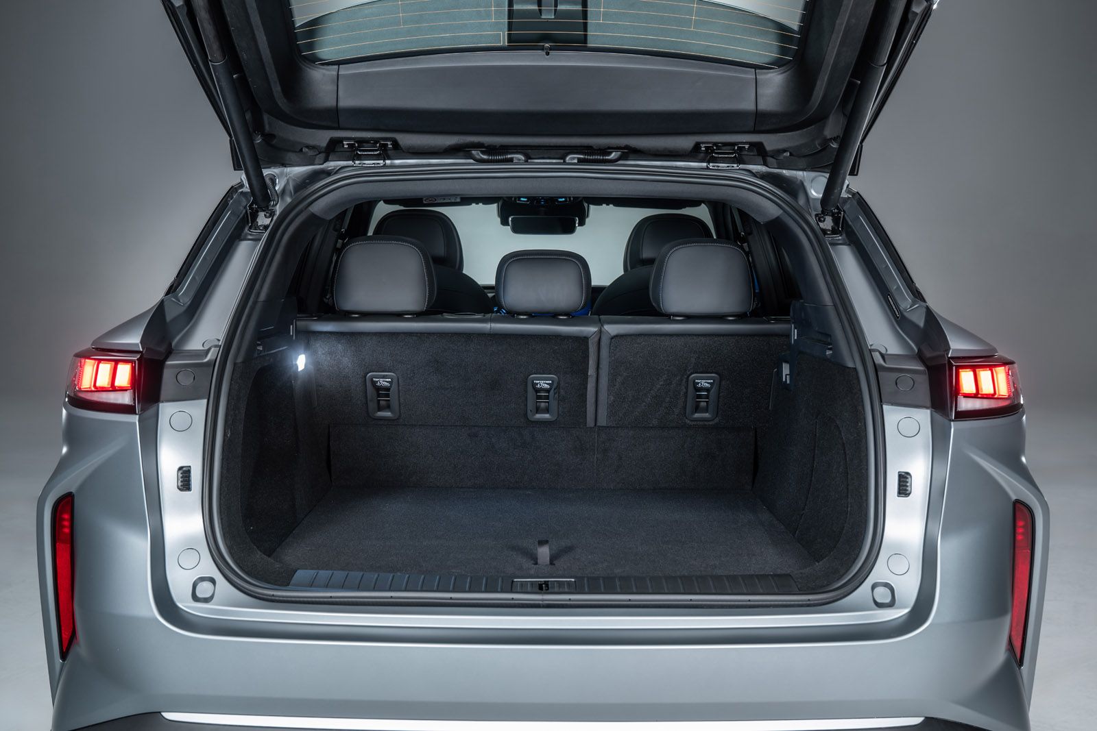 Open trunk of a silver SUV showing spacious cargo area with folded rear seats, illuminated by interior lights.