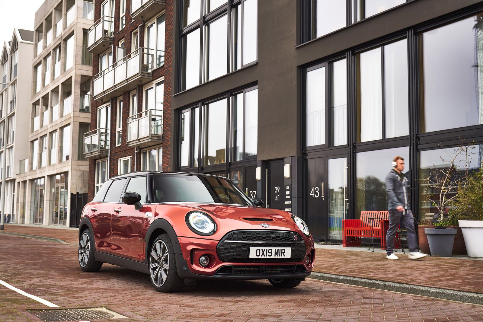 Red Mini Cooper parked on a city street near modern buildings, with a person walking on the sidewalk.