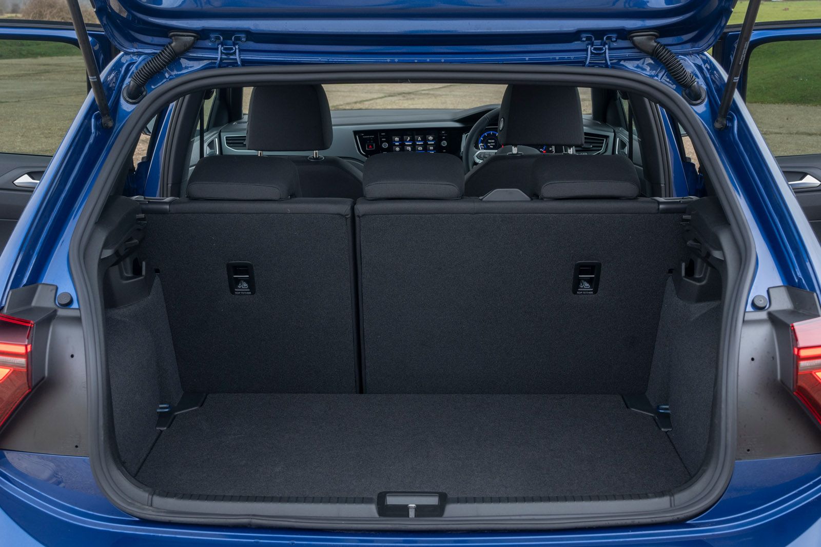 Open trunk of a blue car showing folded rear seats and spacious cargo area with dashboard visible through the rear window.