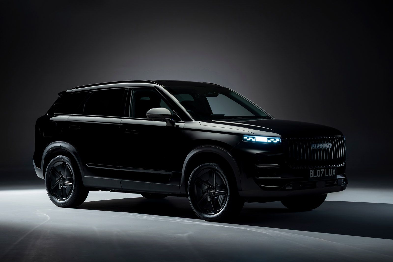 Sleek black SUV in a dimly lit studio, highlighting its modern design, shiny exterior, and illuminated headlights.
