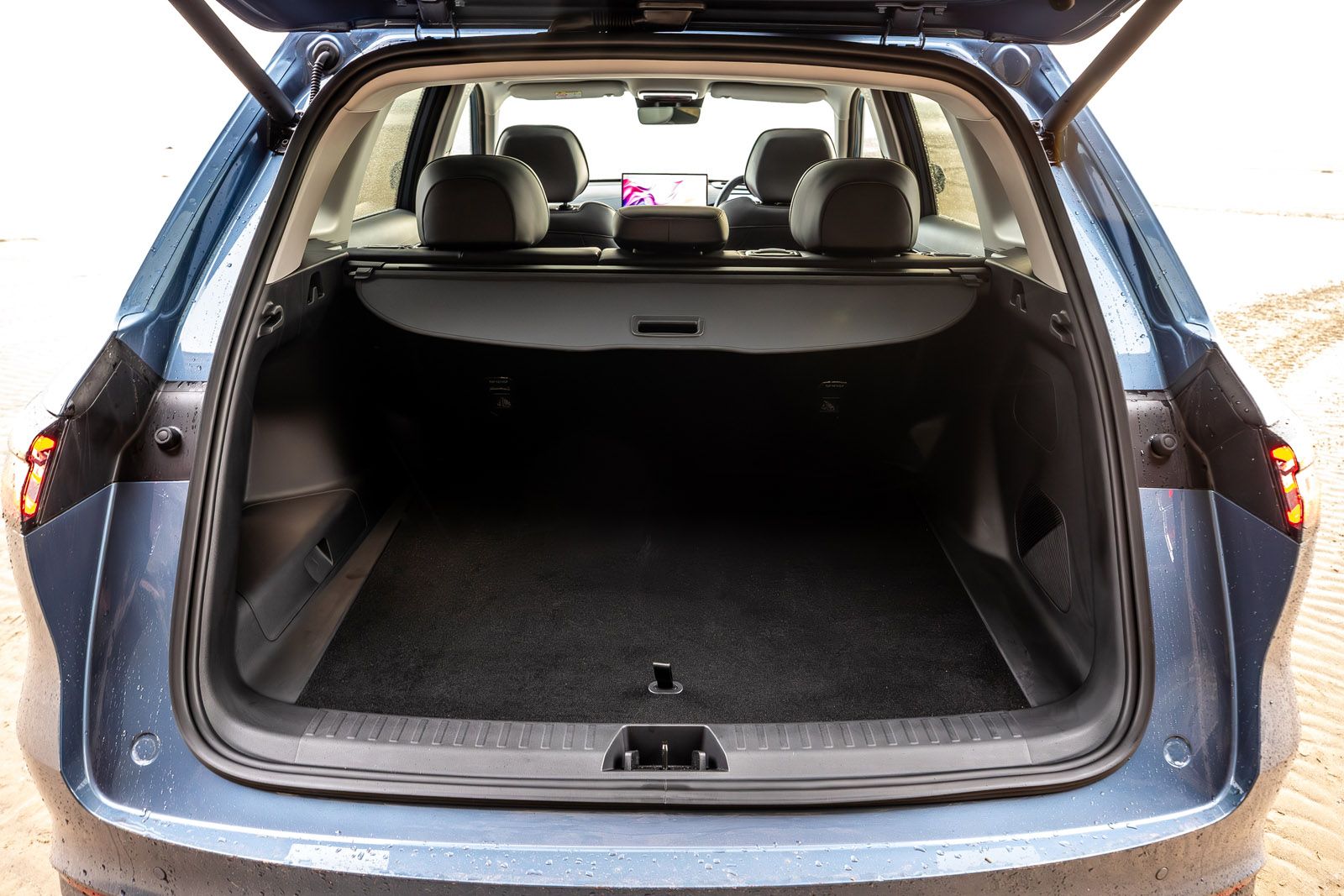 Open trunk of a blue car showing a spacious and clean cargo area, with rear seats and a screen visible in the interior.