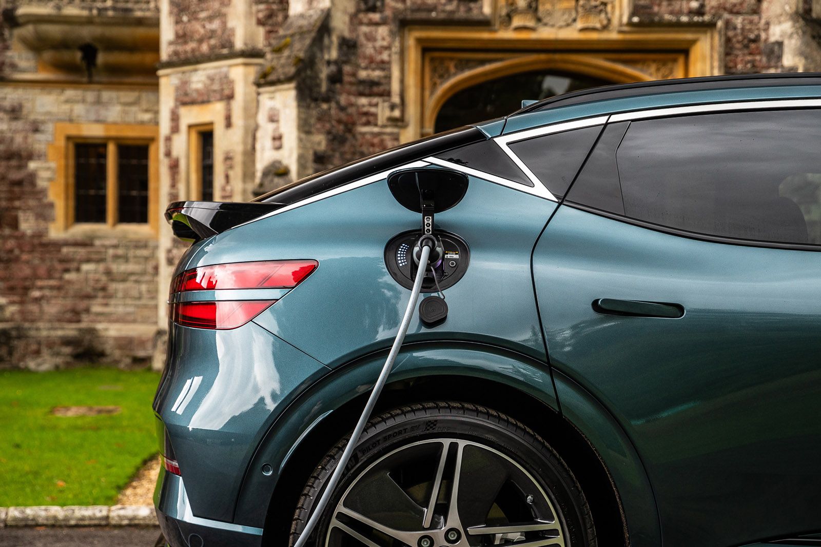 Electric SUV charging outdoors against a historic building backdrop, showing plugged-in cable and sleek vehicle design.