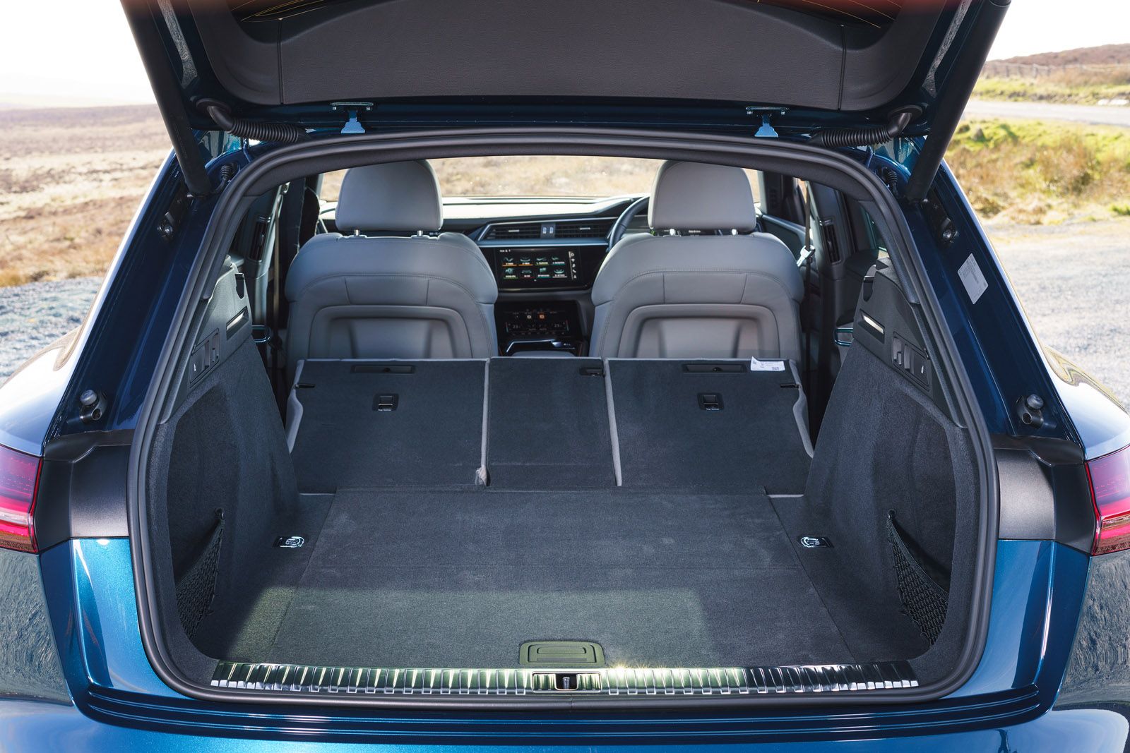 Open trunk of a blue car showing spacious cargo area with rear seats folded down, grey interior, and dashboard visible in the front.