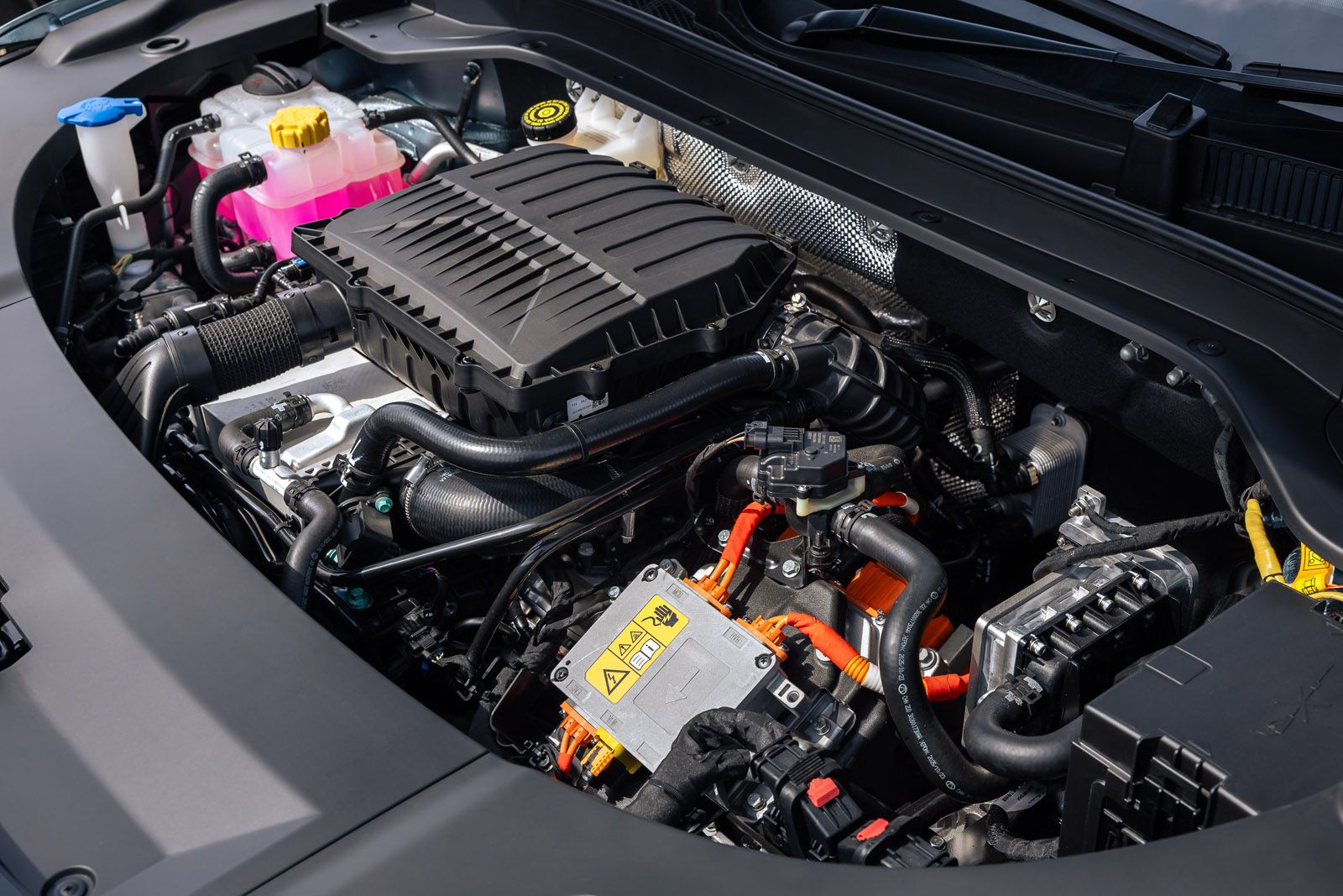 Close-up of a car engine, showing various components, wiring, and a coolant reservoir with pink liquid and a yellow cap.