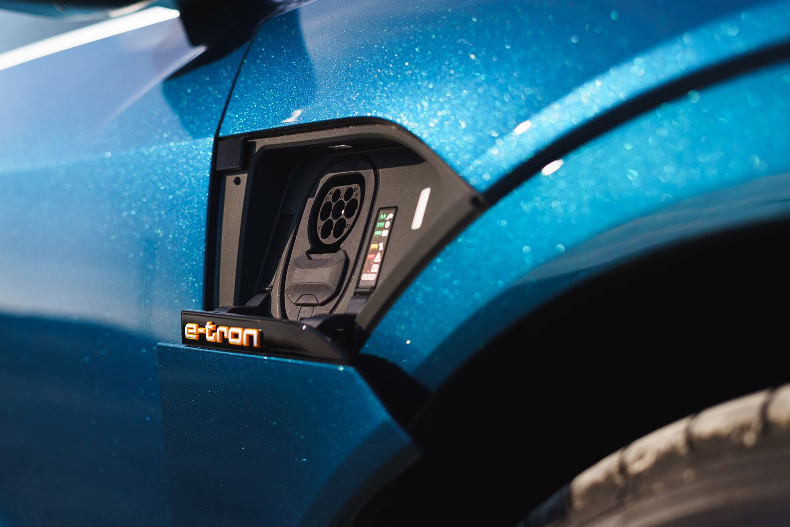 Close-up of a blue electric car's charging port, featuring the e-tron logo and a plug-in socket.