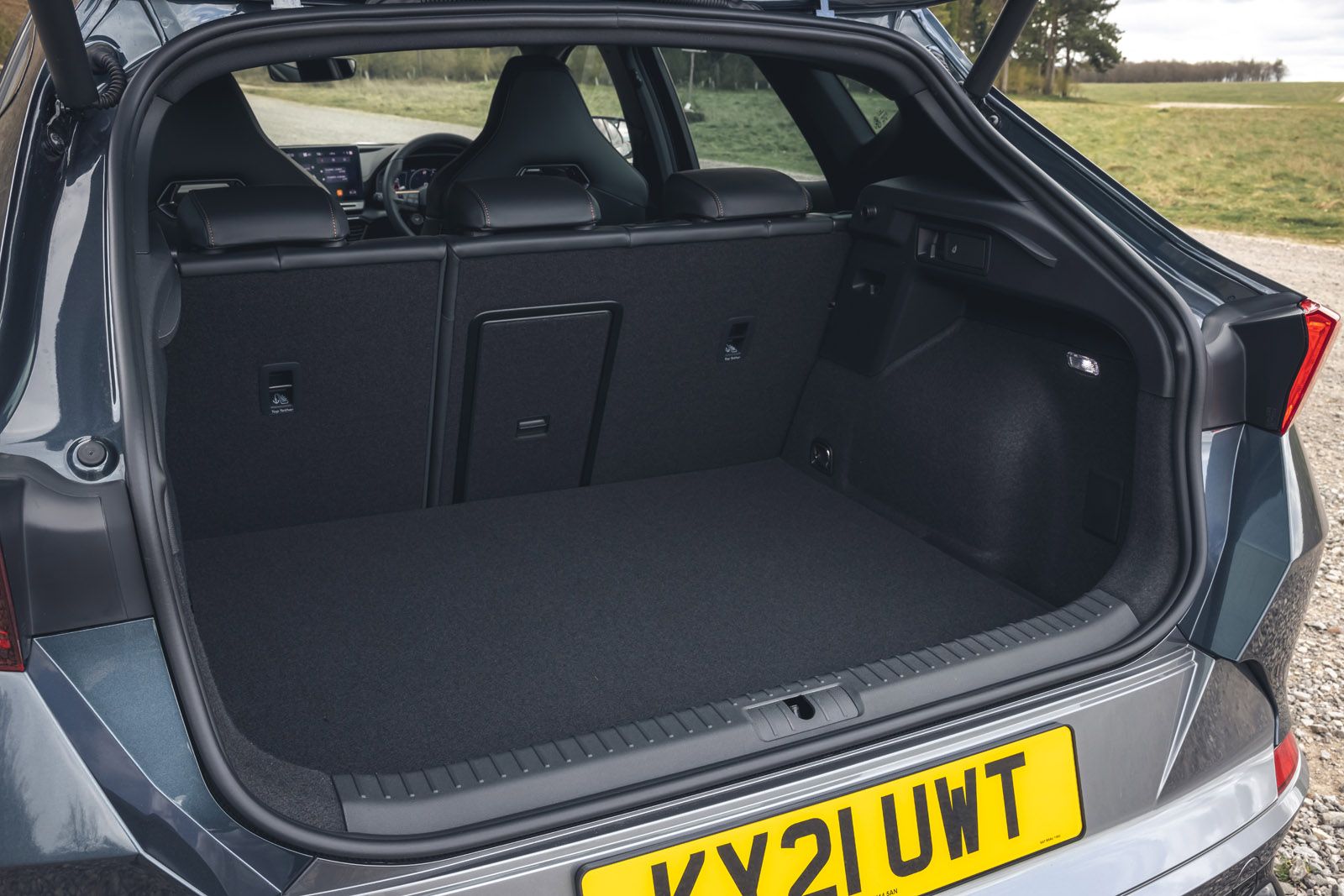 Car trunk with seats folded down, showing spacious cargo area and rear seats. License plate visible, grassy field in the background.