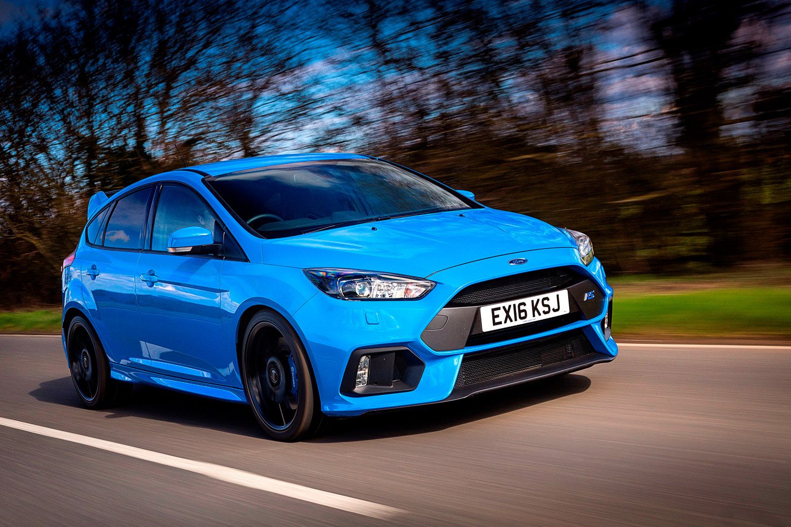 Blue sporty car driving fast on a road, surrounded by blurred trees, in motion. License plate reads "EX16 KSJ."