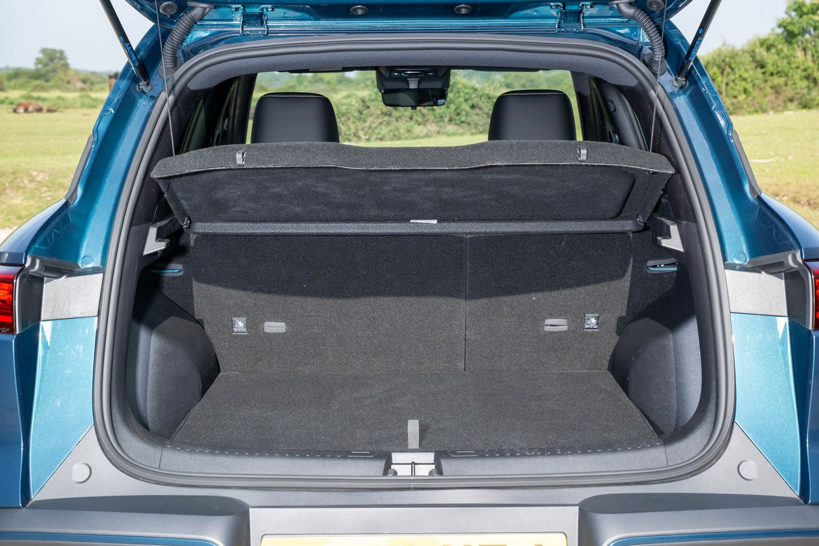 Open trunk of a blue SUV, showing spacious cargo area with split-fold rear seats, set against a grassy outdoor background.