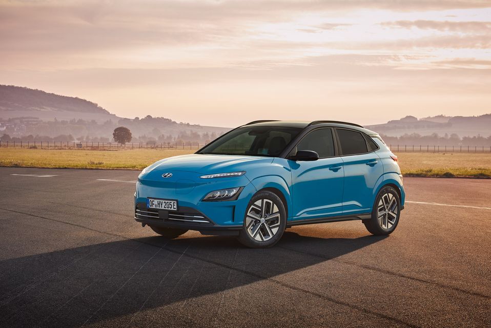 Blue SUV parked on a paved road with mountains and a hazy sky in the background at sunrise or sunset.
