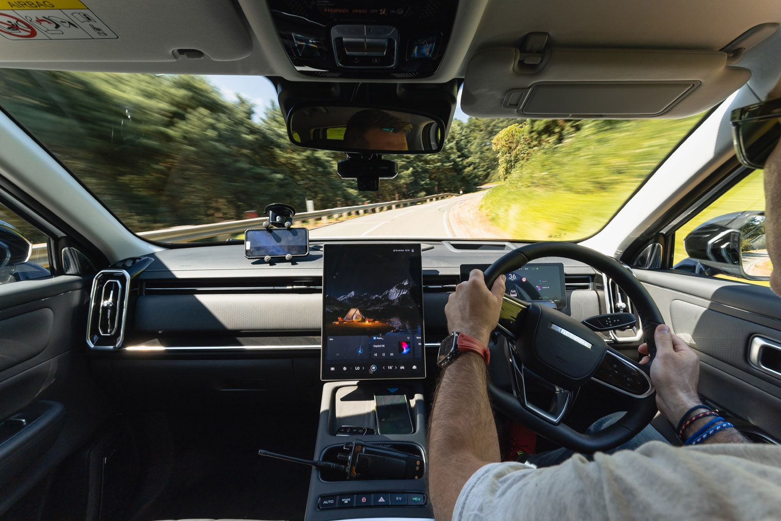 Driver's view from inside a modern car, showcasing a digital dashboard and trees blurred outside, suggesting motion.