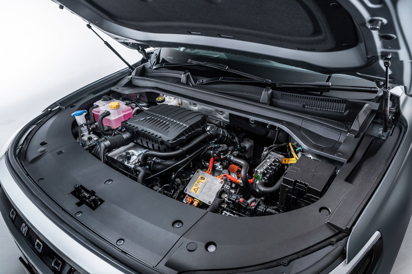 The open hood of a modern car showing a neatly arranged and clean engine with various components, wires, and fluid containers visible.