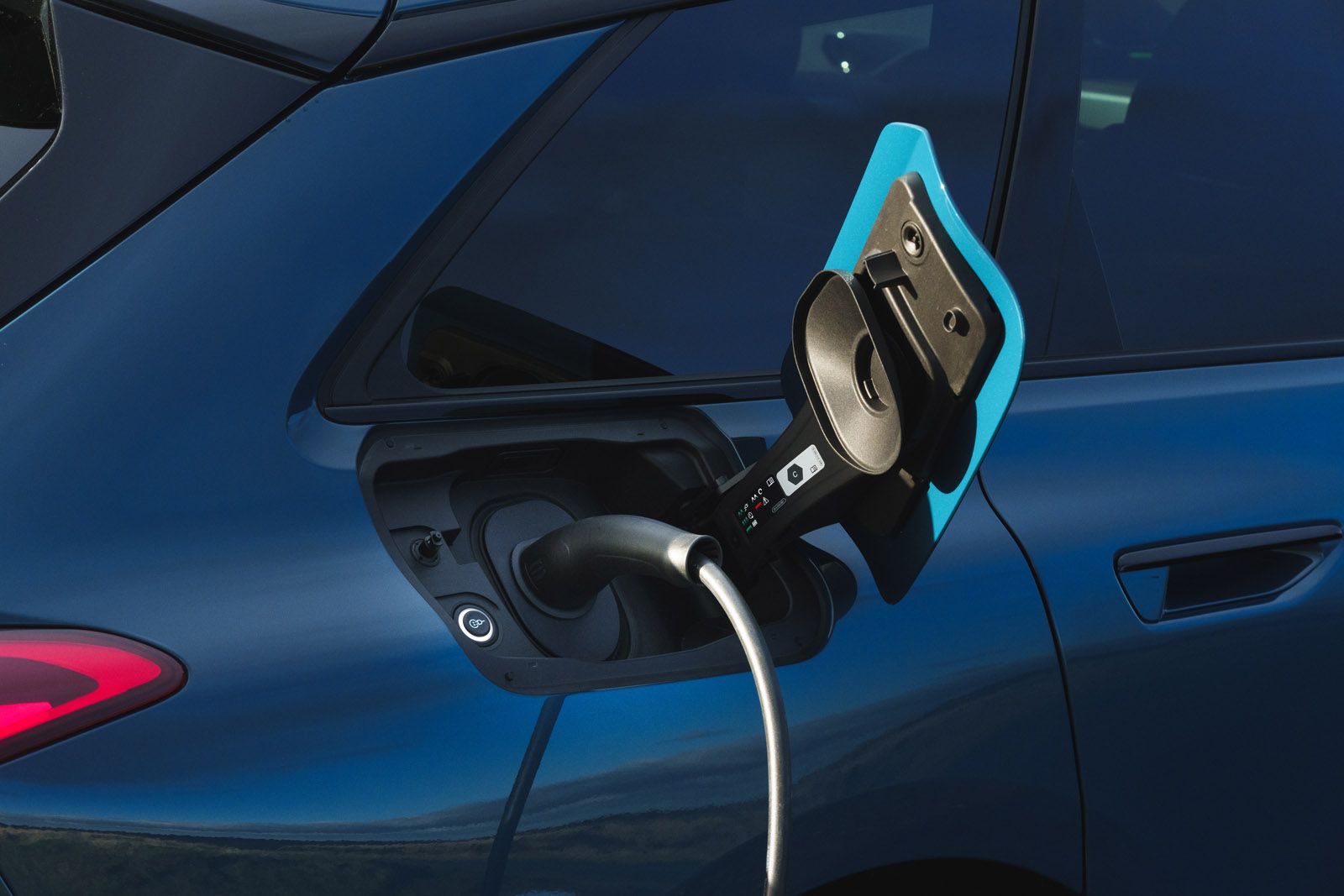 Electric vehicle charging, blue car with charging cable connected to the port on the side of the vehicle.