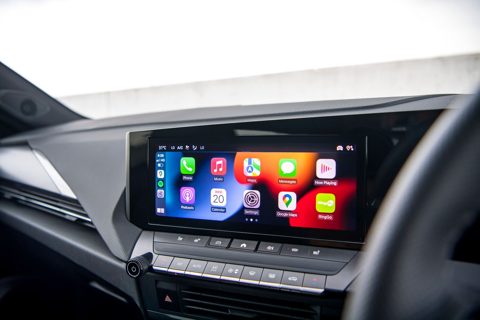 Car interior screen displaying apps like Phone, Music, Maps, and Messages. Climate control buttons and dashboard visible below.