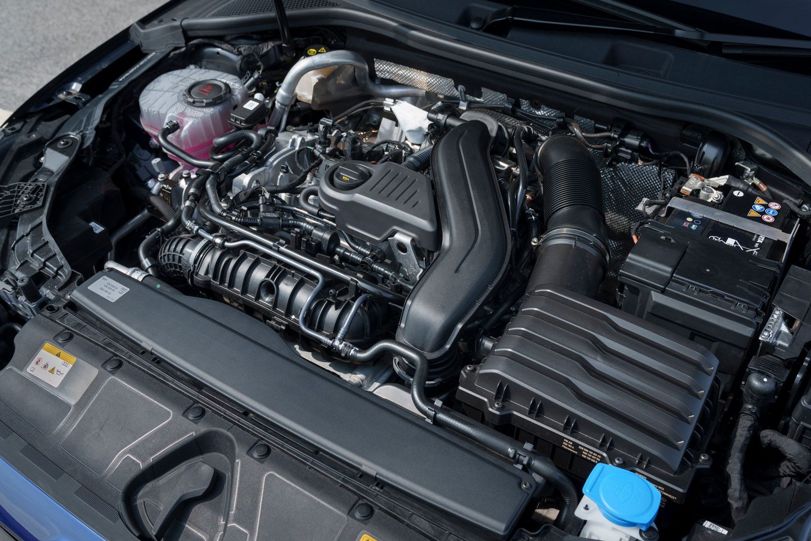 Close-up of a car engine with various components visible, including belts, hoses, and a black plastic engine cover, within a clean engine bay.