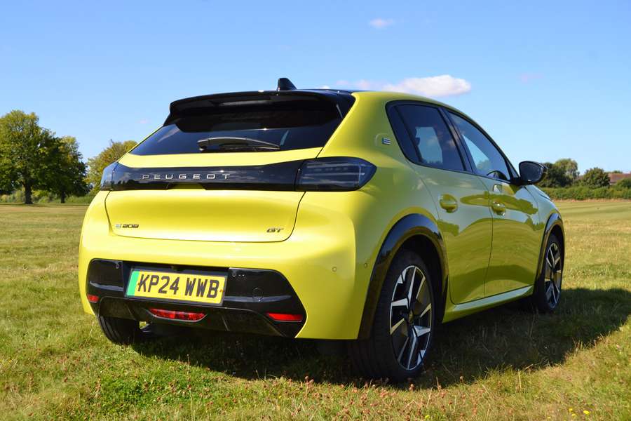 Bright yellow Peugeot 208 GT car parked on grass under a clear blue sky, rear view showing license plate and sleek design.