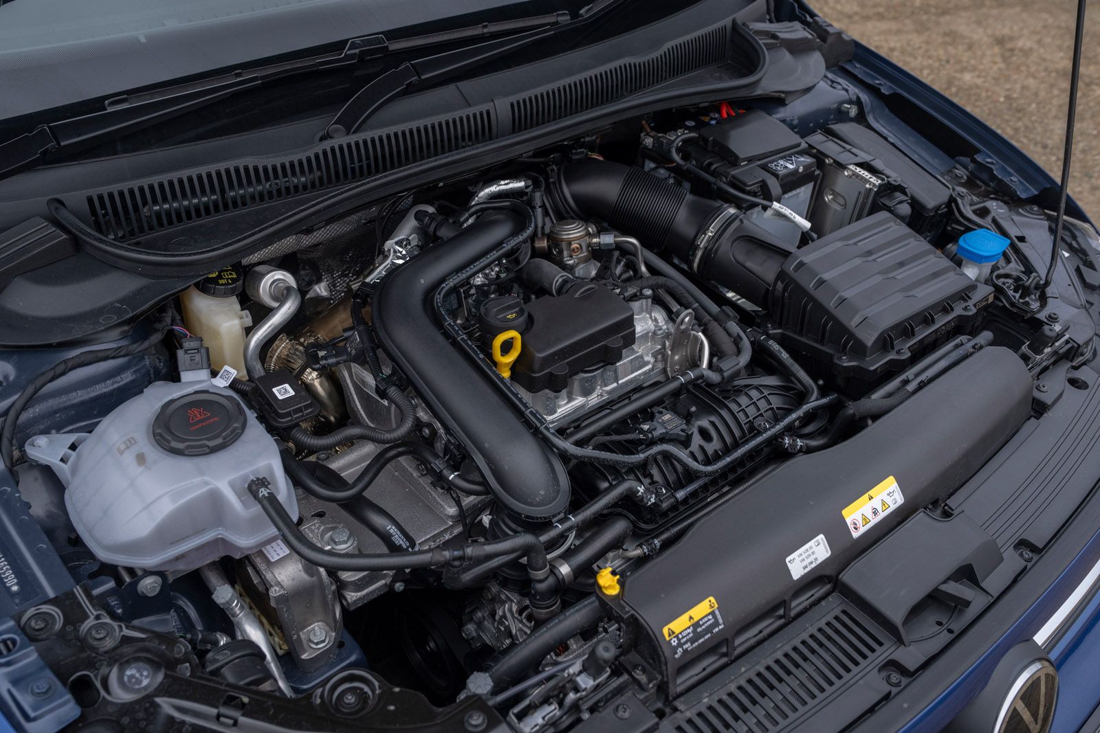 Close-up of a car engine compartment showing various components, hoses, and fluid reservoirs.
