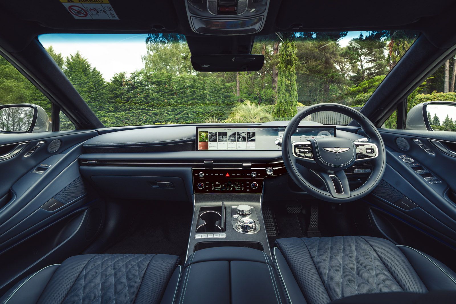 Luxury car interior with a sleek dashboard, large touchscreen display, elegant black leather seats, and a view of trees through the windshield.