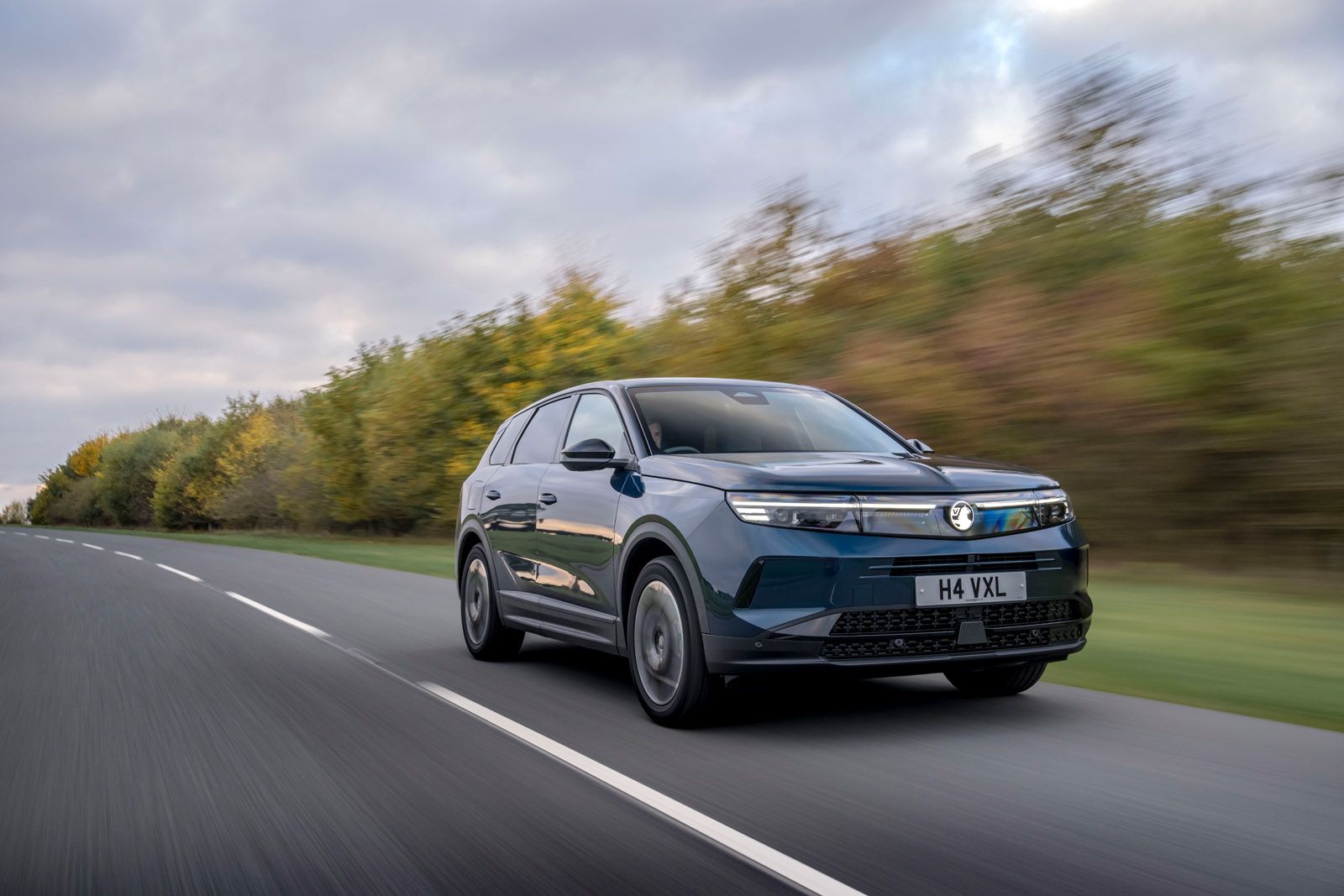 A sleek black SUV driving on a road with blurred trees in the background, under a cloudy sky.