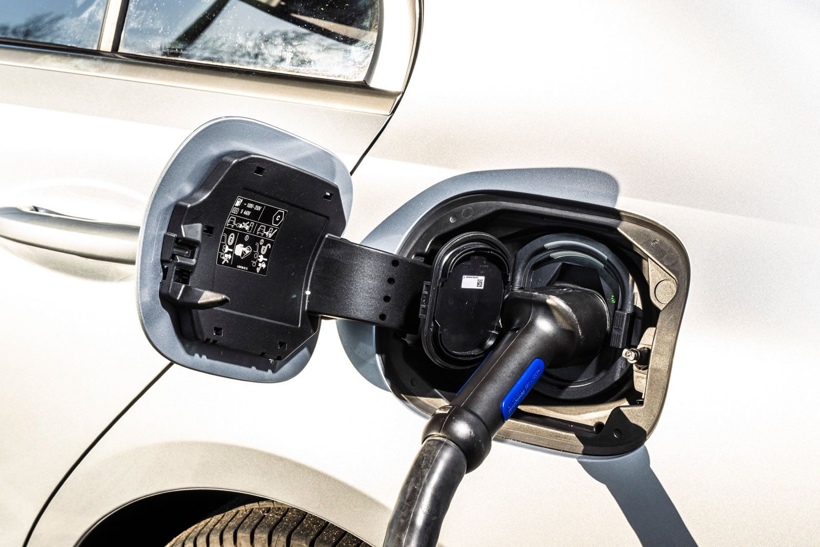 Close-up of an electric vehicle being charged, showing the charging port and plugged-in cable on a silver car.