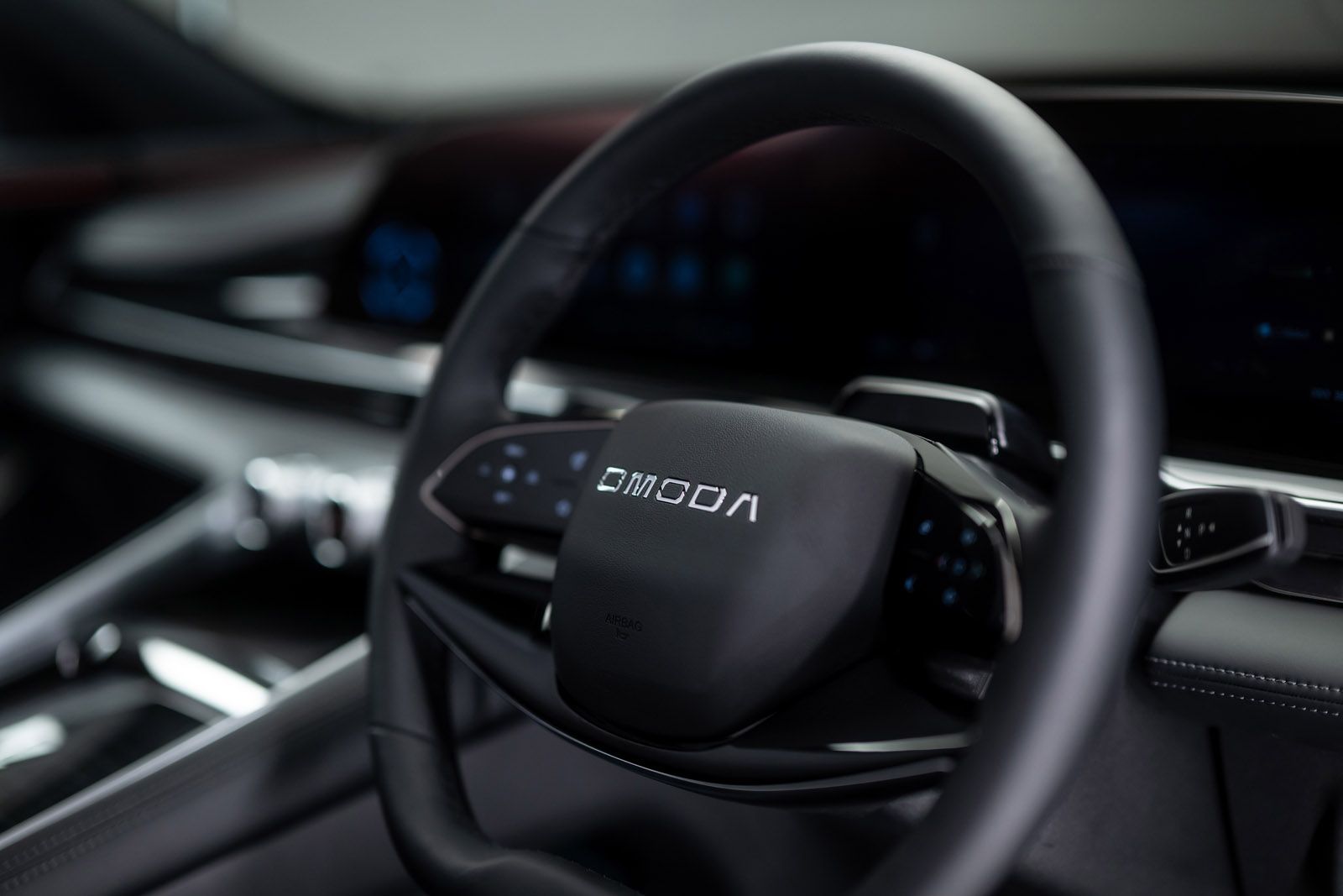 Close-up of a car's steering wheel featuring a digital display and sleek dashboard design, with the brand "Omoda" visible on the wheel.