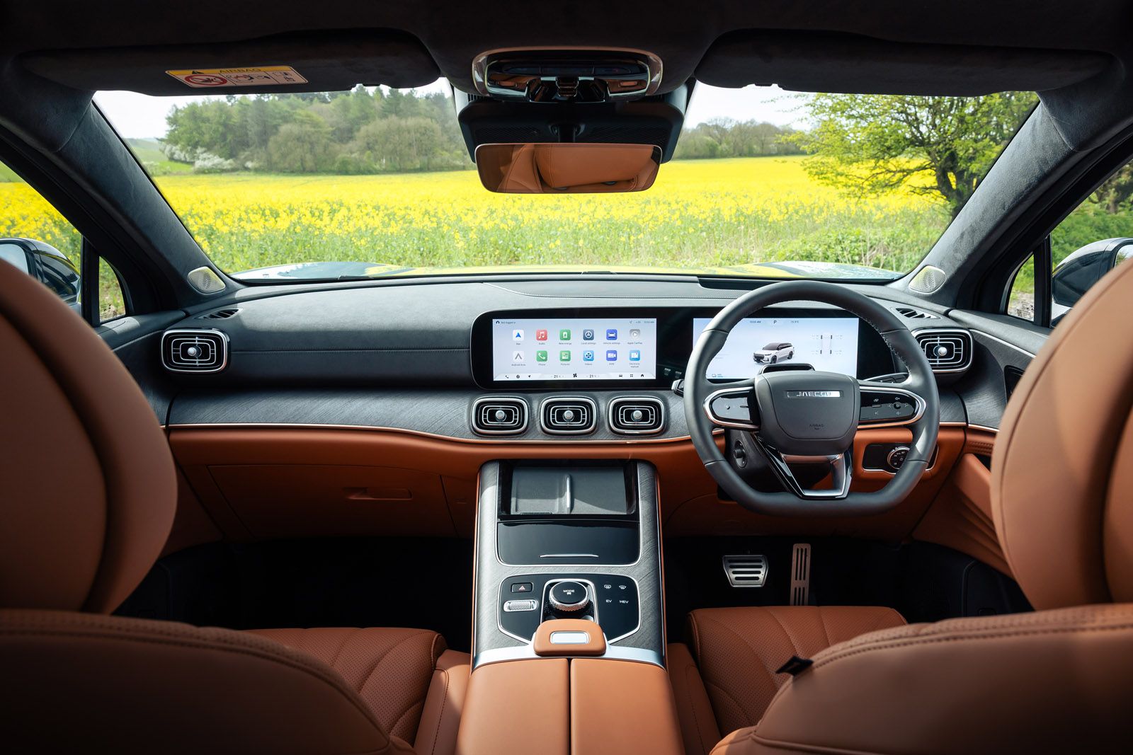 Luxury car interior with tan leather seats, modern dashboard, and digital screens, set against a scenic view of a yellow flower field.