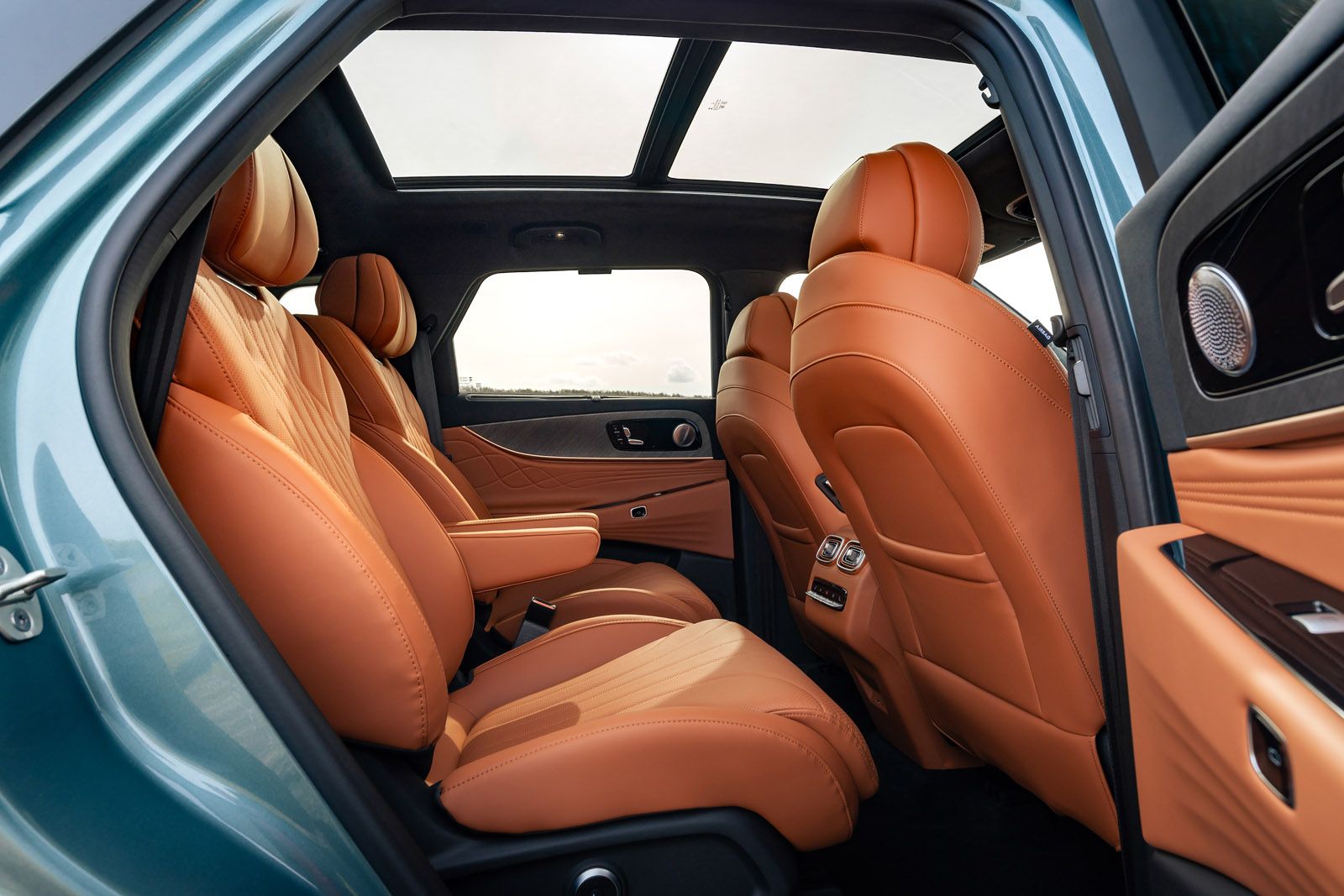 Luxury car interior with tan leather seats and a panoramic sunroof, viewed from the rear passenger side door.