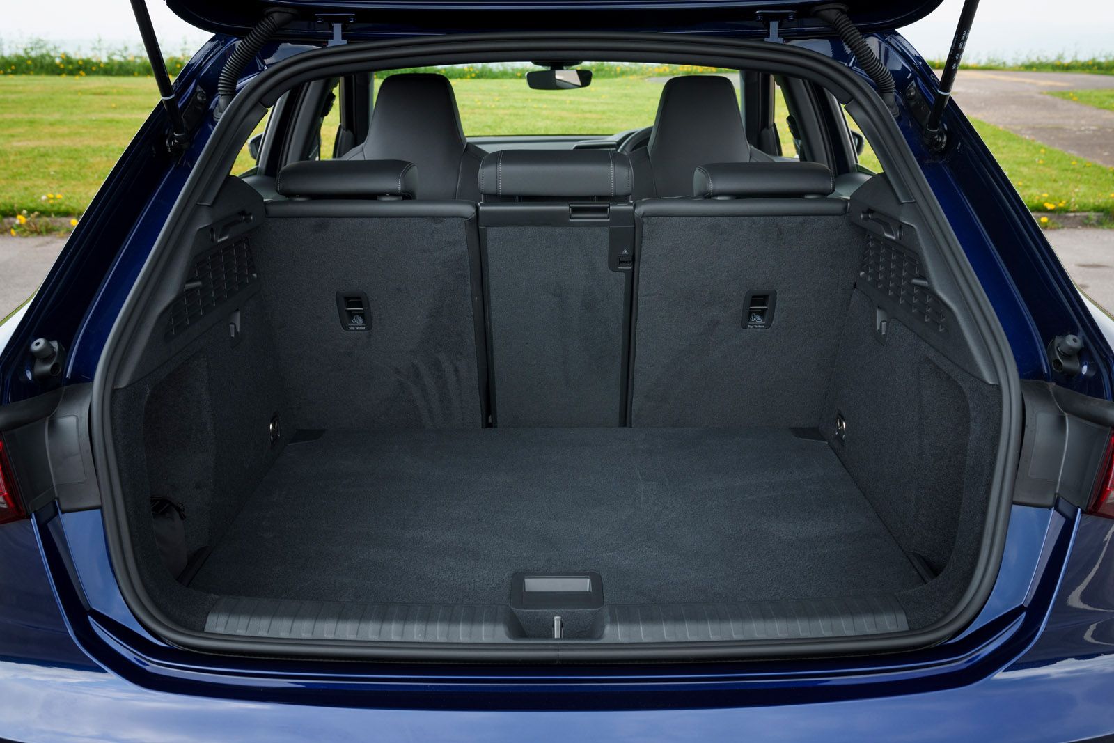 Open trunk of a blue car with rear seats folded down, showcasing a spacious cargo area, parked in a grassy area.