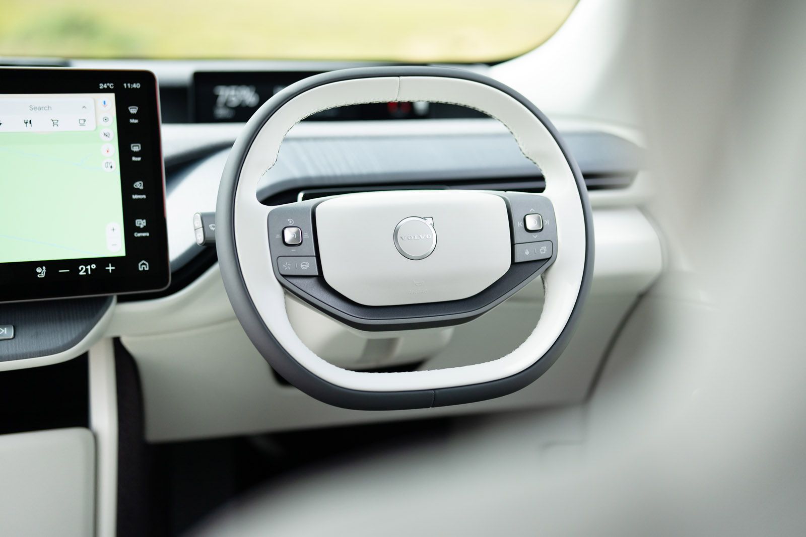 Close-up of a car's steering wheel with control buttons, next to a digital display showing navigation and climate settings.