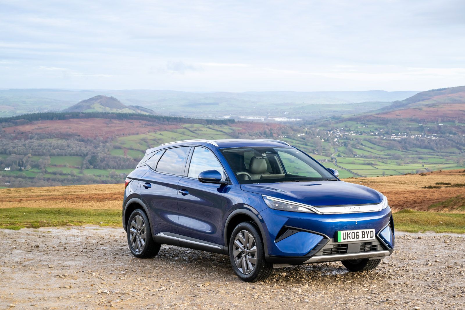 Blue SUV parked on a gravel path with rolling hills and a cloudy sky in the background.
